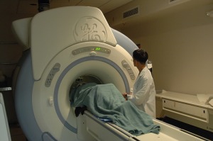 Person under sheet having MRI medical test with medical personnel watching.