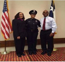 Two people in business attire stand with their daughter, wearing a police uniform.