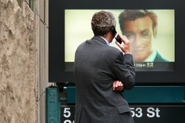 Man talks on cell phone looking at big picture of a man.